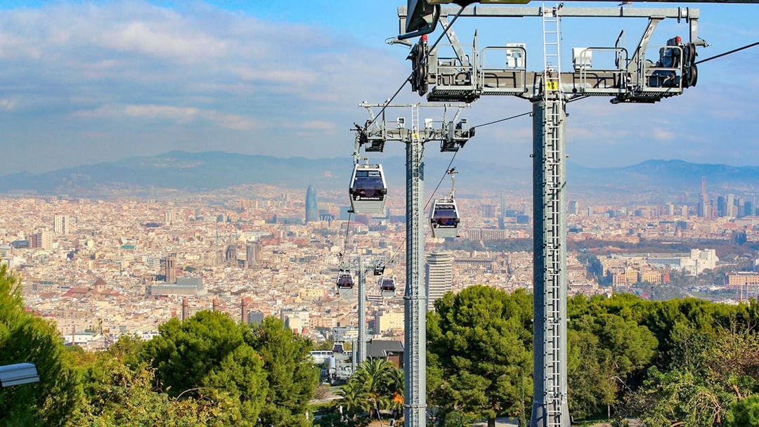 Cable cars ascending Montjuic with Barcelona cityscape in the background.
