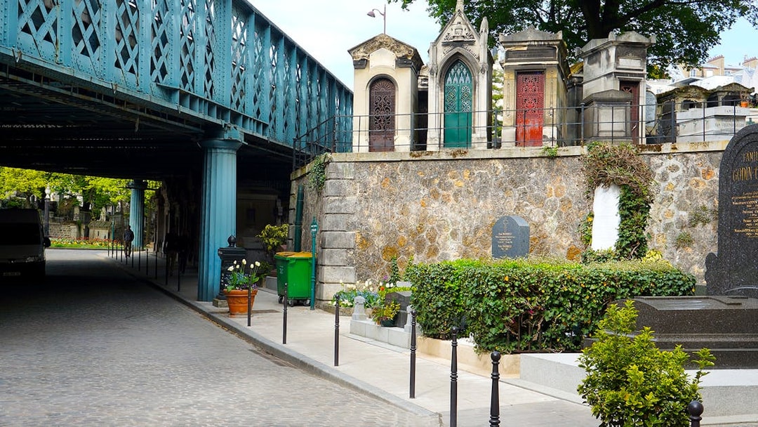 Montmartre Cemetery under bridge in Paris, featuring ornate tombs and greenery.