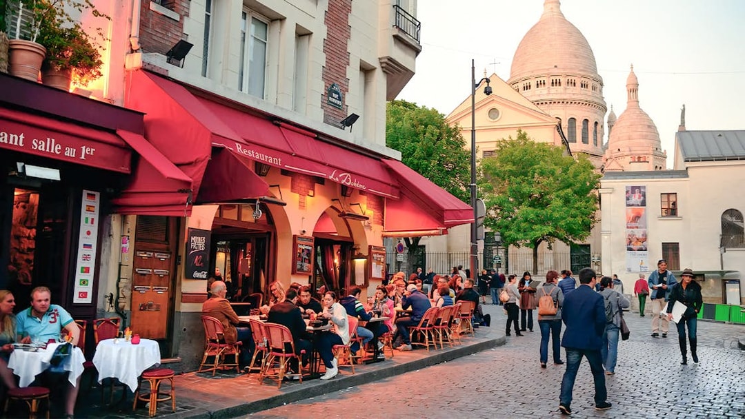 Outdoor dining at a restaurant in Montmartre, Paris, with Sacré-Cœur Basilica in the background.