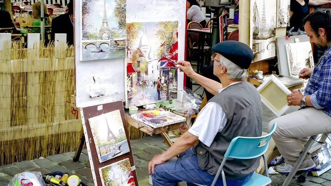 Artist painting street scene in Montmartre, Paris with Eiffel Tower artwork displayed.
