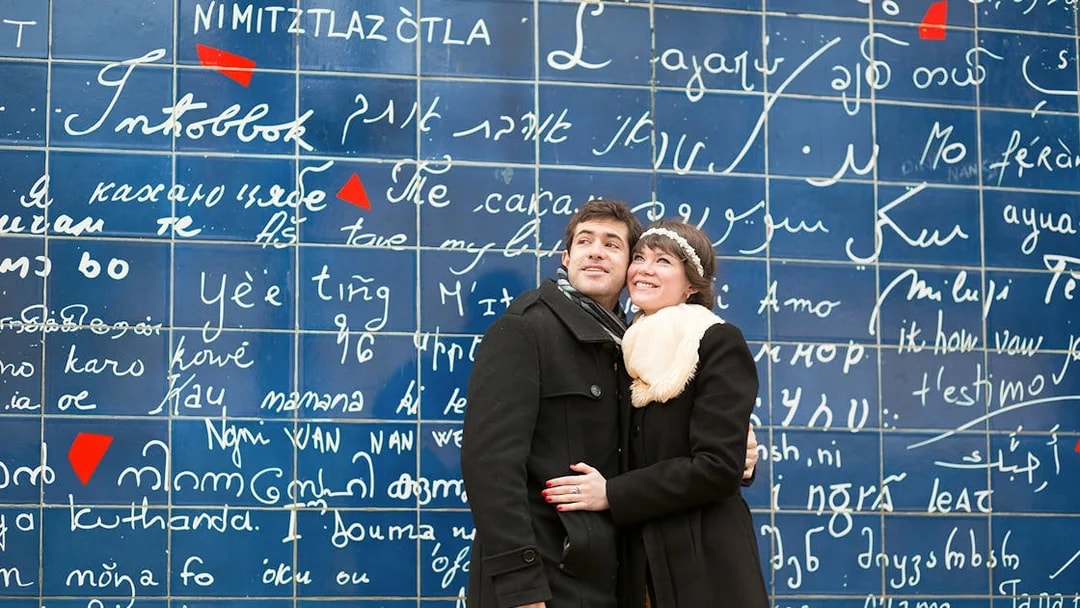 Couple standing in front of the Wall of Love in Montmartre, Paris.