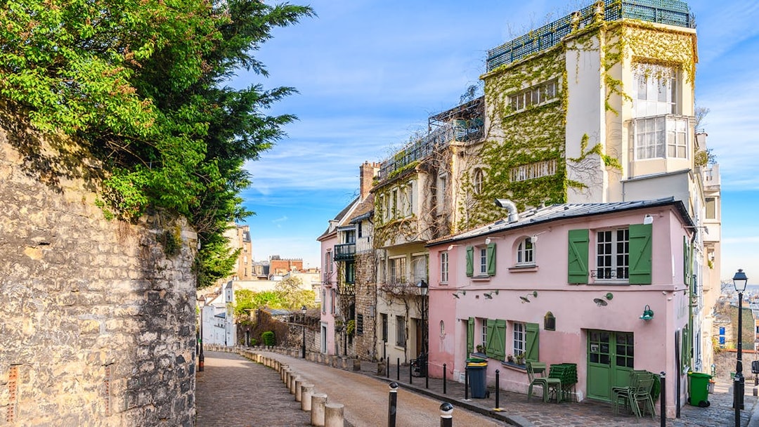 Cobblestone street in Montmartre, Paris, lined with ivy-covered buildings and a pink café.
