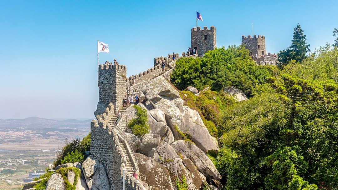 Moorish Castle on hilltop with visitors, overlooking Sintra's lush landscape, Portugal.