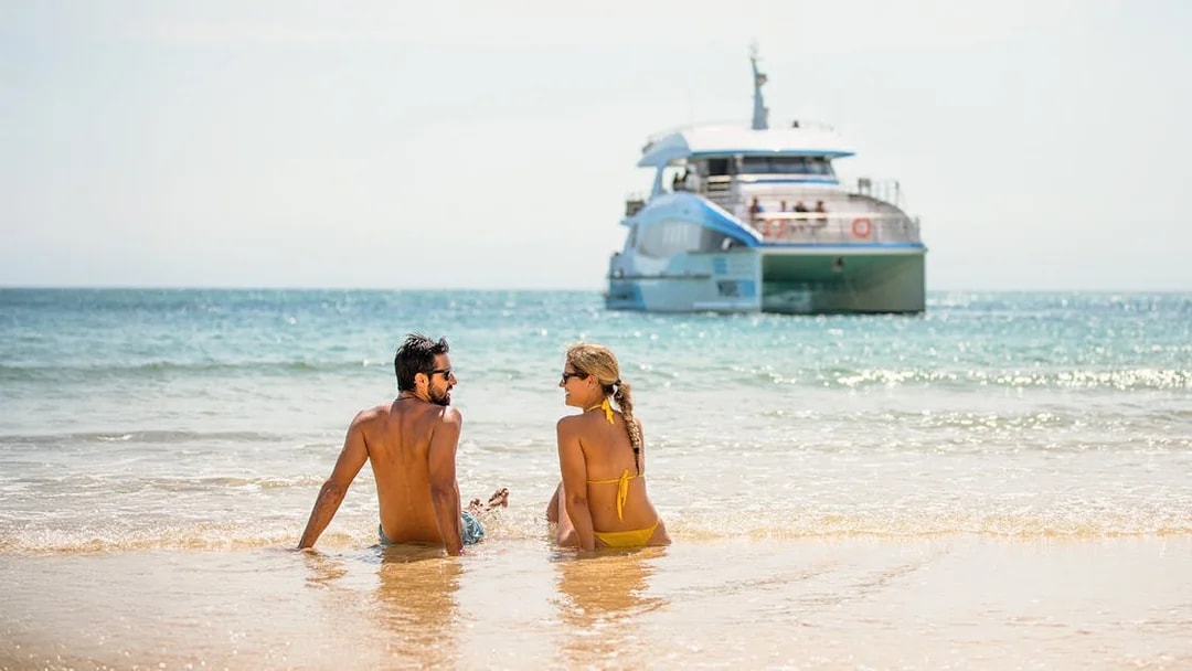 Couple sitting on Moreton Island beach with a boat in the background.