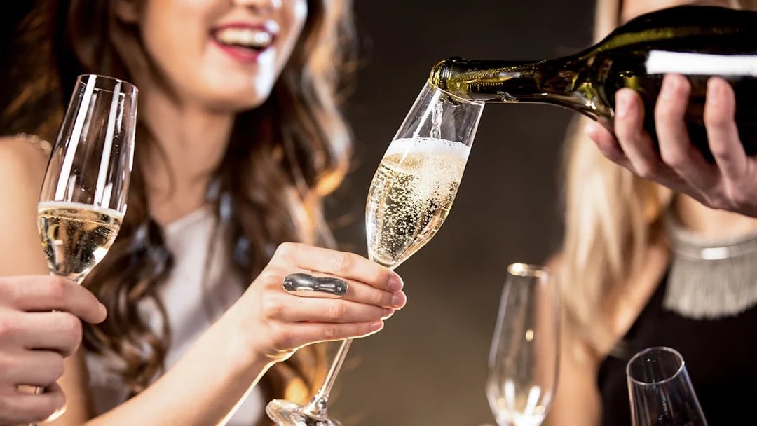 Barista pouring Champagne into a glass at a social gathering.