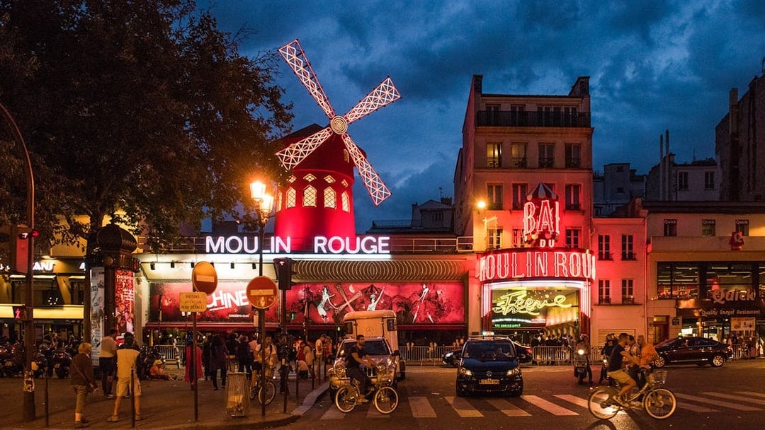 Panoramic view of Moulin Rouge exterior in Paris at night with illuminated windmill.