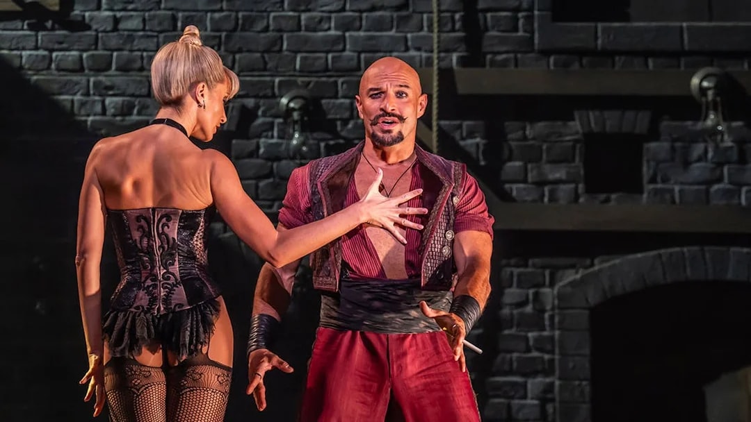Performers on stage during Moulin Rouge! The Musical, with a dramatic brick backdrop.