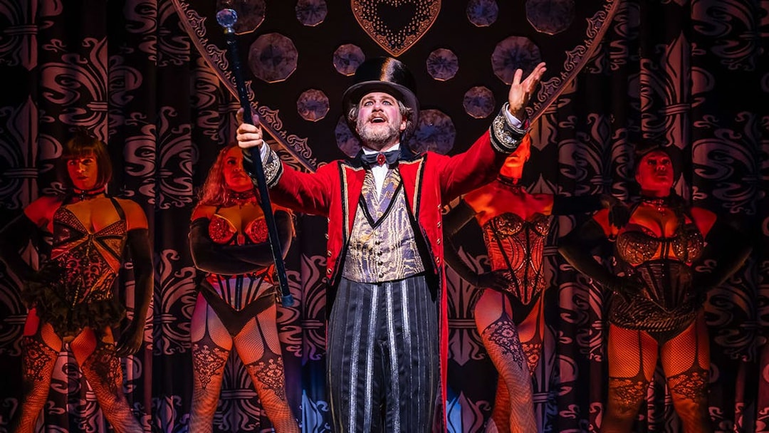 Performer in red coat with dancers at Moulin Rouge! The Musical stage show.
