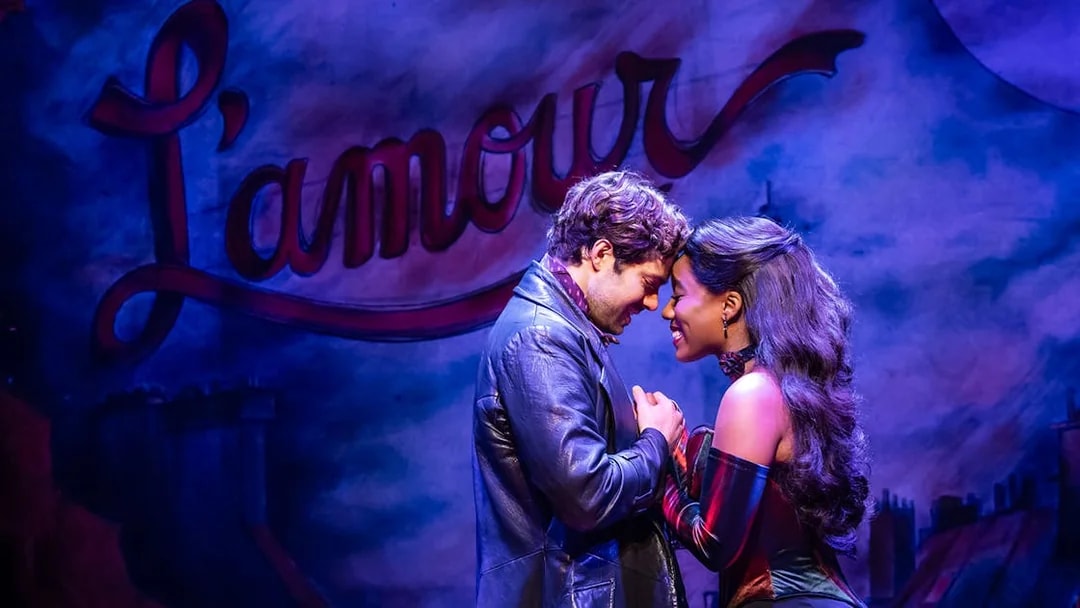 Actors embrace on stage during Moulin Rouge! The Musical with "L'amour" in the background.