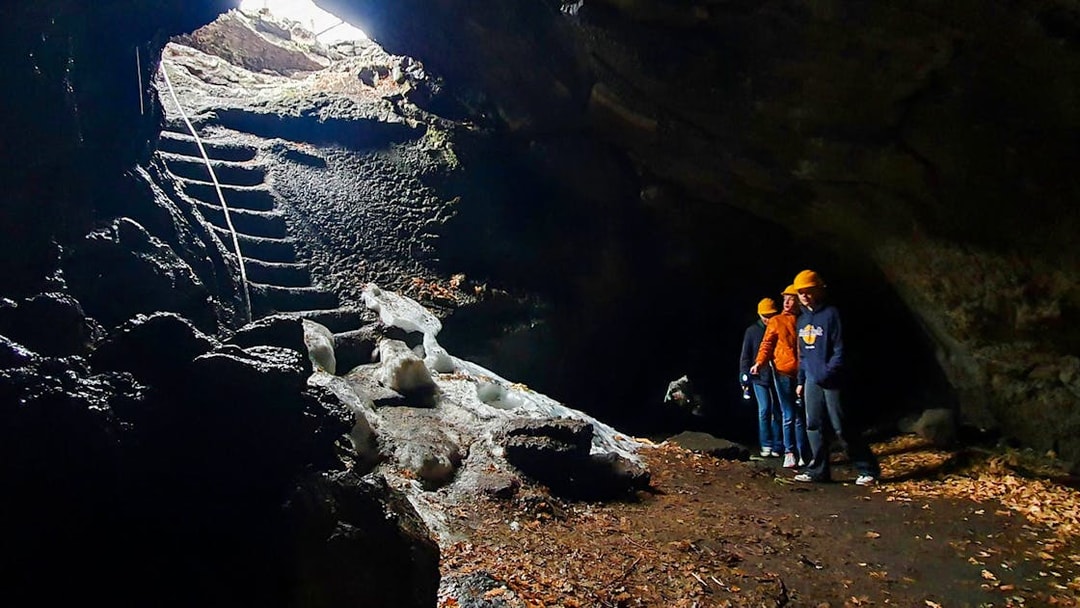 Visitors exploring a cave on Mount Etna with helmets and flashlights.
