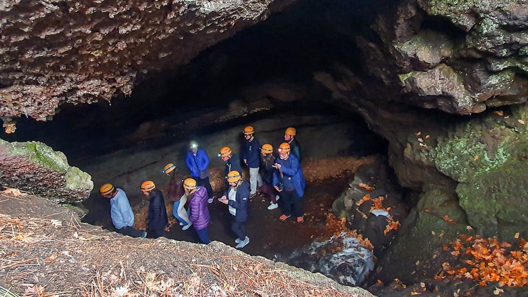 Group exploring a cave on Mount Etna tour, wearing helmets and jackets.