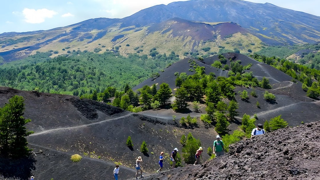 Hikers exploring volcanic terrain on Mount Etna with lush greenery in the background.