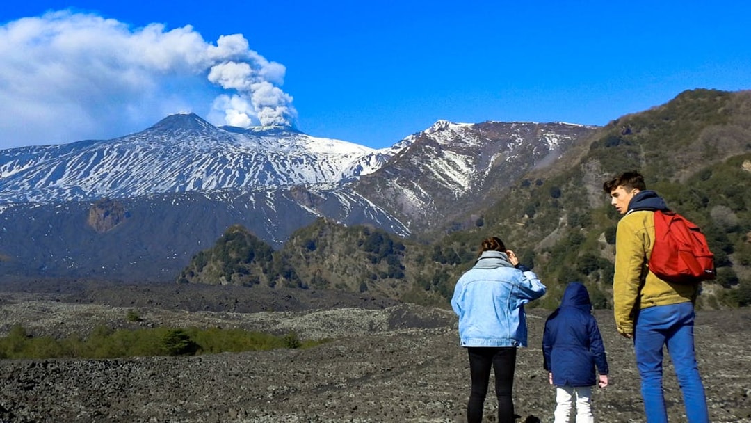 Hikers exploring volcanic landscape of Mount Etna with smoke rising from the crater.