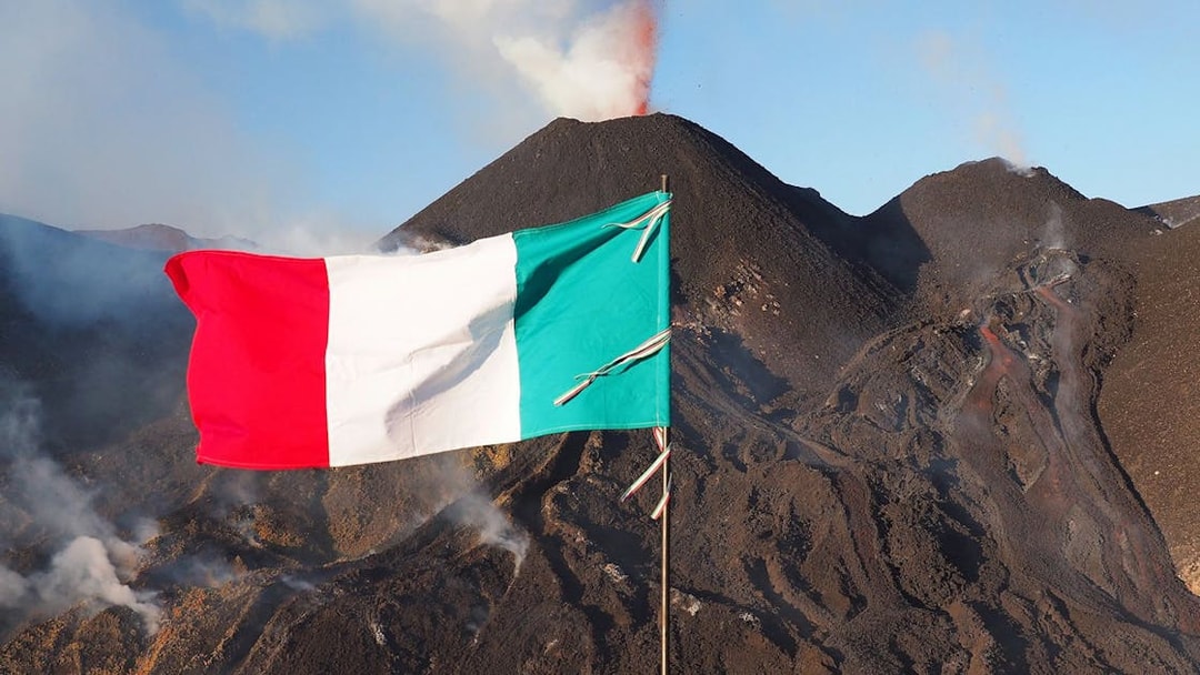 Italian flag waving in front of Mount Etna with smoke, Sicily, Italy.