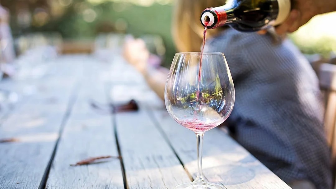 Wine being poured into a glass on a wooden table during Mount Etna tour.