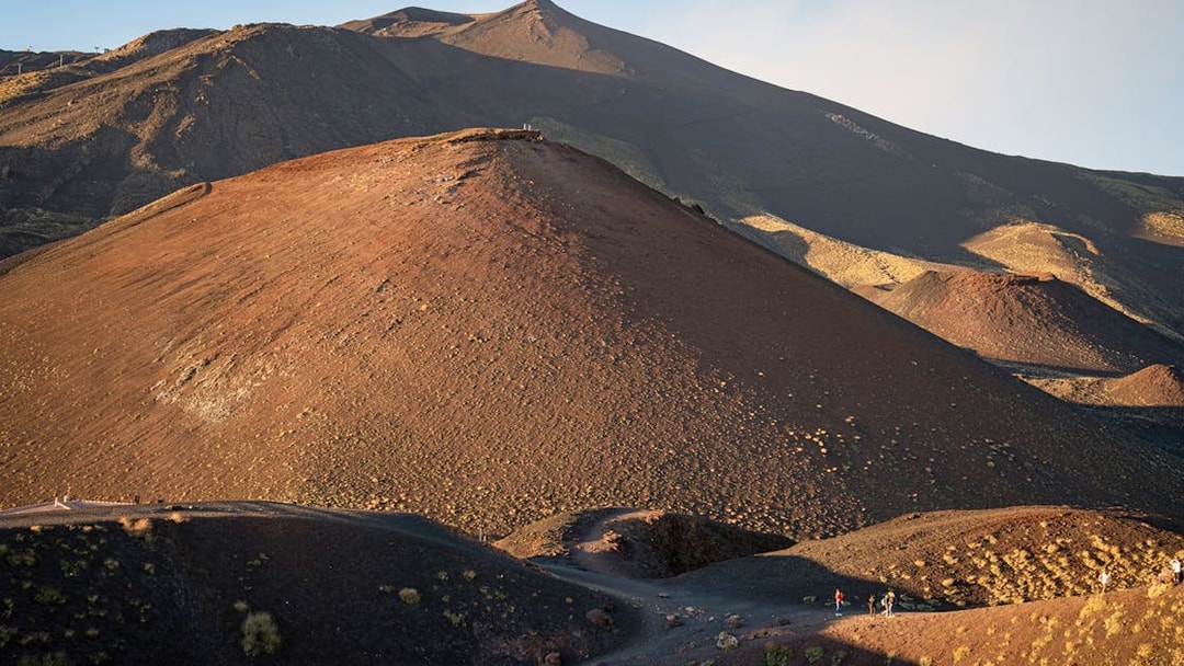 Mount Etna's volcanic landscape at sunset with hikers on the trail.