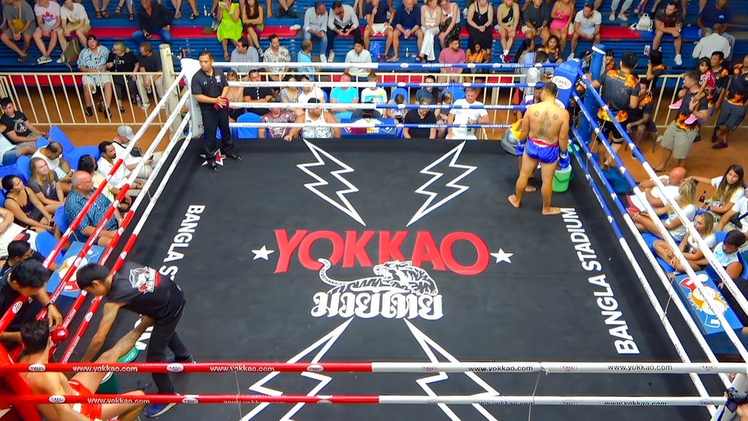 Muay Thai match at Bangla Boxing Stadium with a fighter in the ring and audience watching.