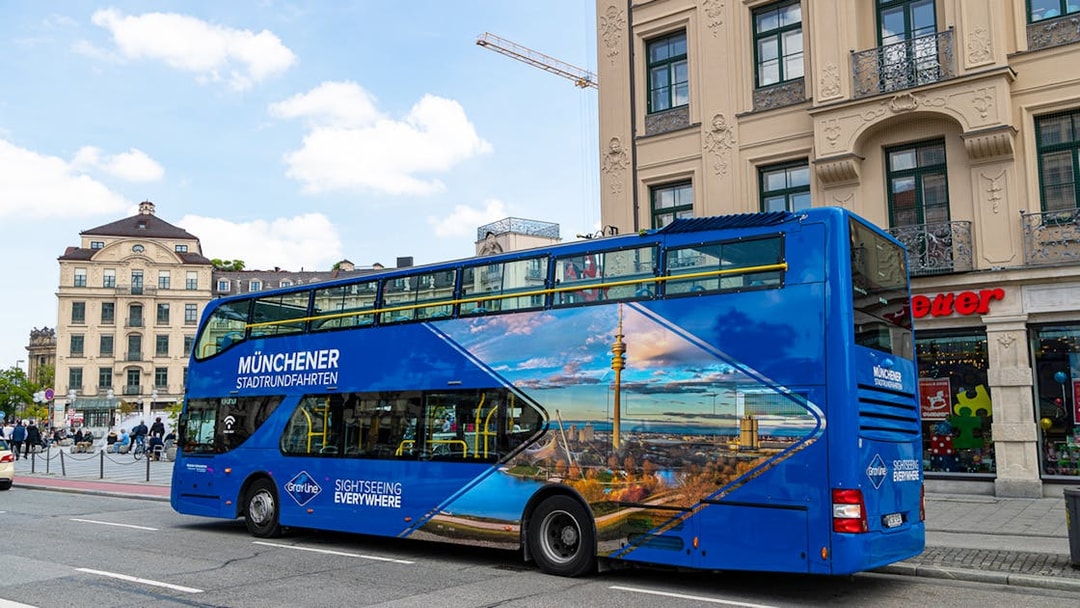 Blue double-decker tour bus in Munich city center, promoting city and FC Bayern Munich Arena tours.
