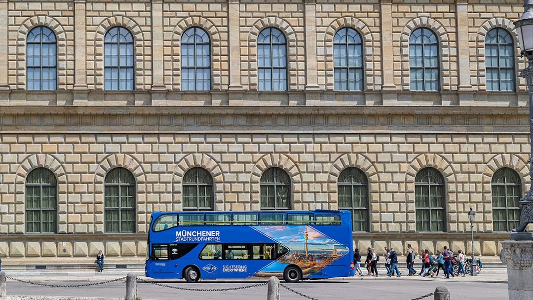 Blue double-decker tour bus in front of Munich's historic building on Hop-On/Hop-Off Express Tour.