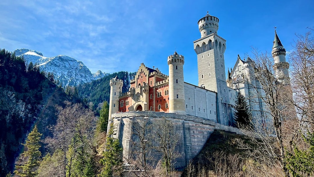 Neuschwanstein Castle with mountain backdrop, part of Munich train tour.