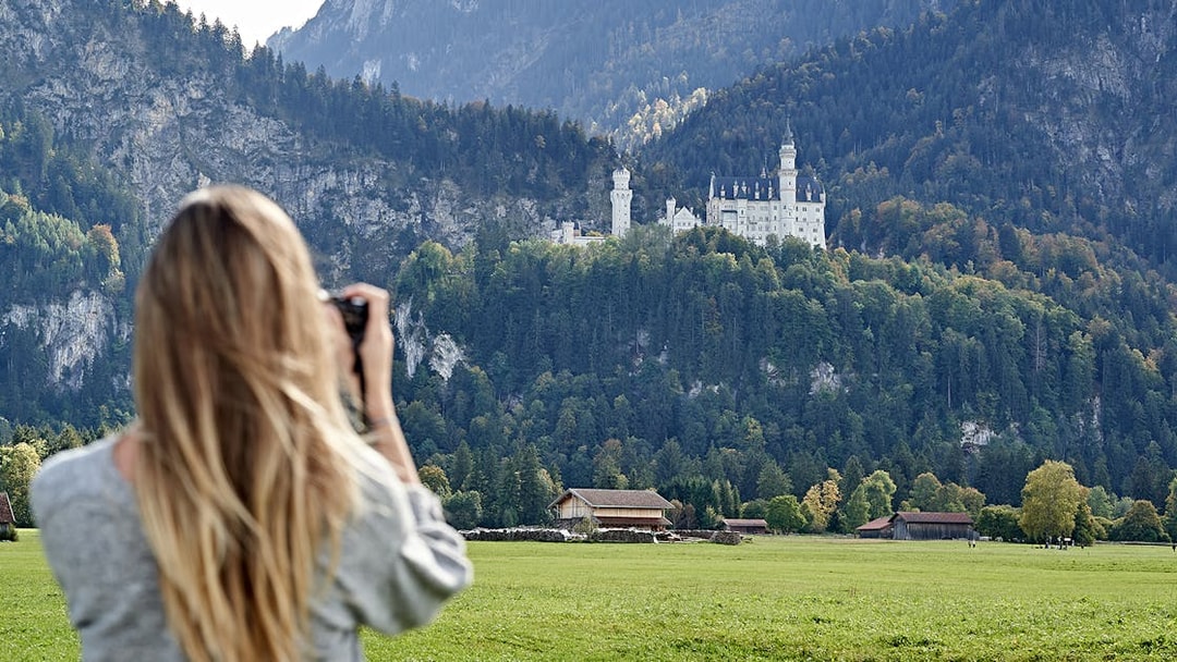 Person photographing Neuschwanstein Castle from a field, Bavaria, Germany.