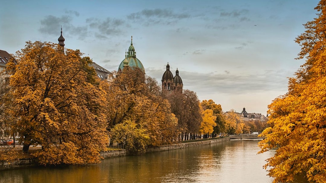 Munich river view with autumn trees and historic buildings, part of Neuschwanstein tour.