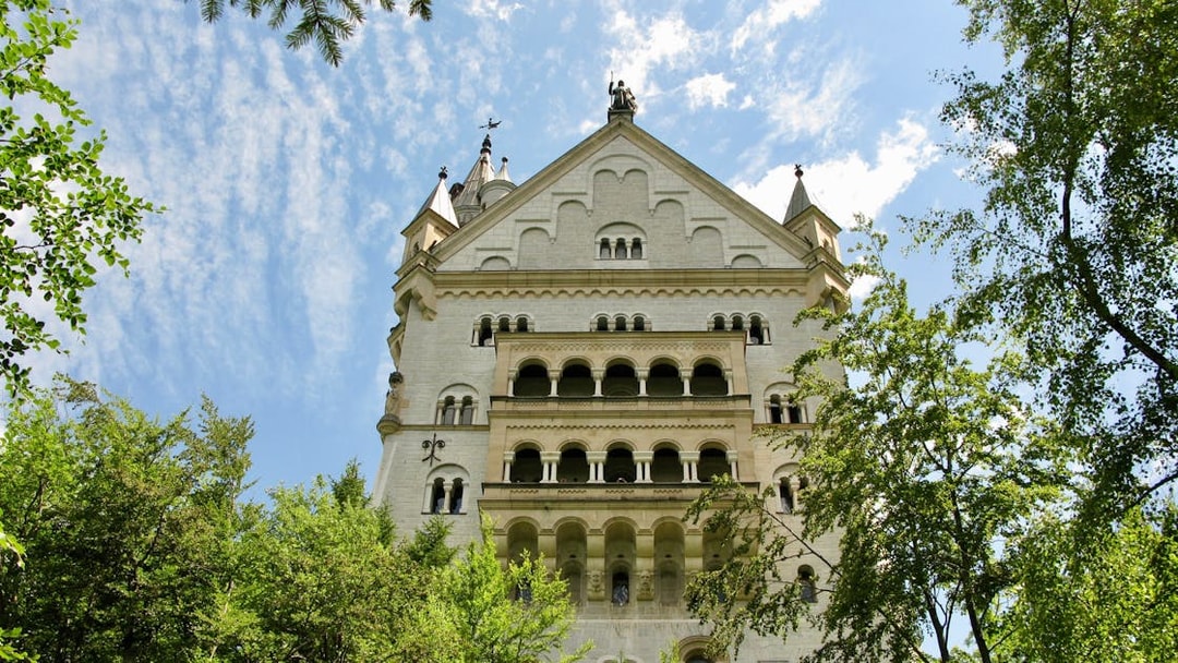 Neuschwanstein Castle facade surrounded by trees, viewed from below, Bavaria, Germany.