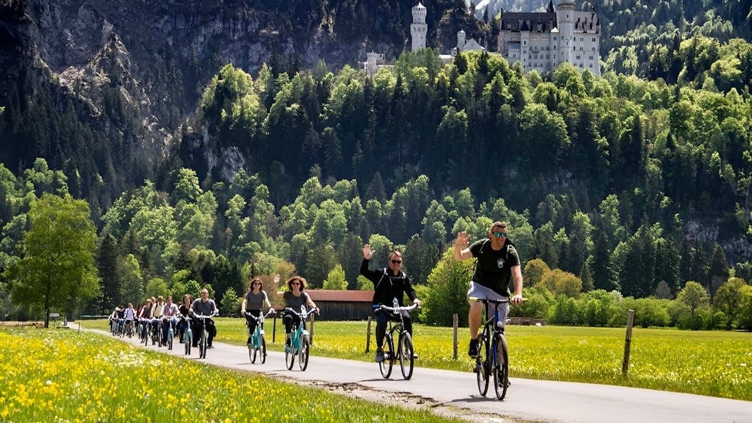 Cyclists on a path with Neuschwanstein Castle in the background, summer tour from Munich.