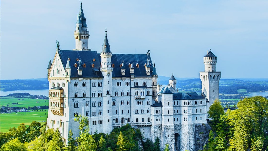 Neuschwanstein Castle in Bavaria, Germany, surrounded by lush greenery and distant hills.