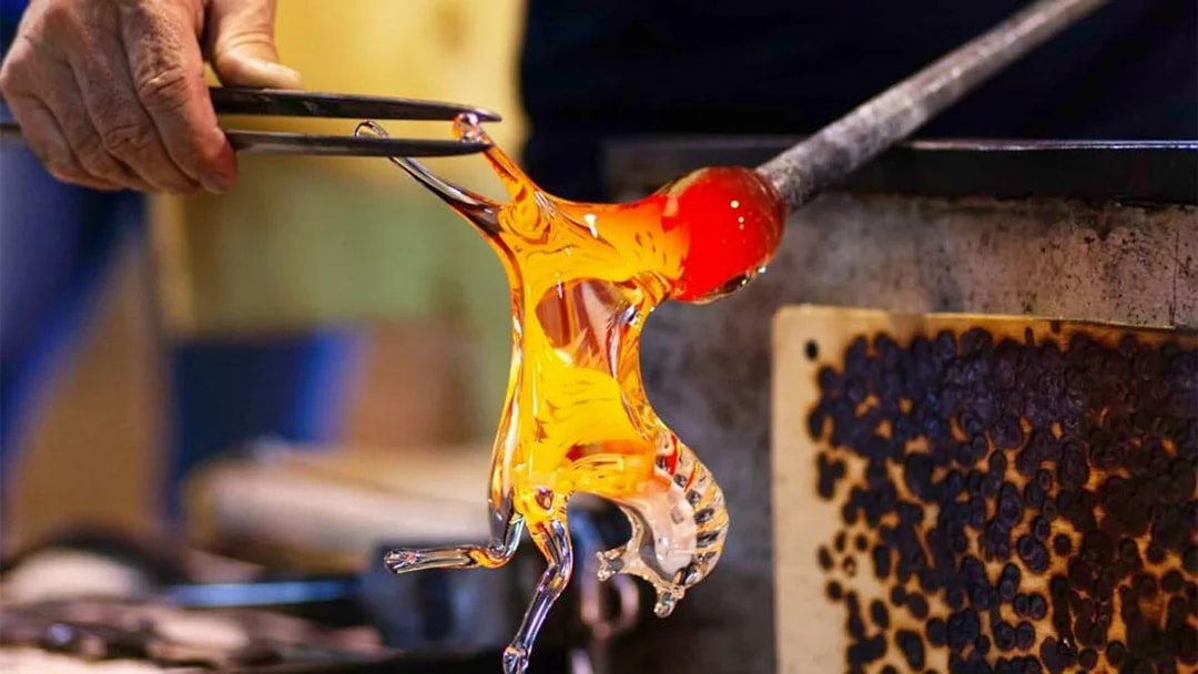 Glass artisan shaping molten glass in Murano workshop.