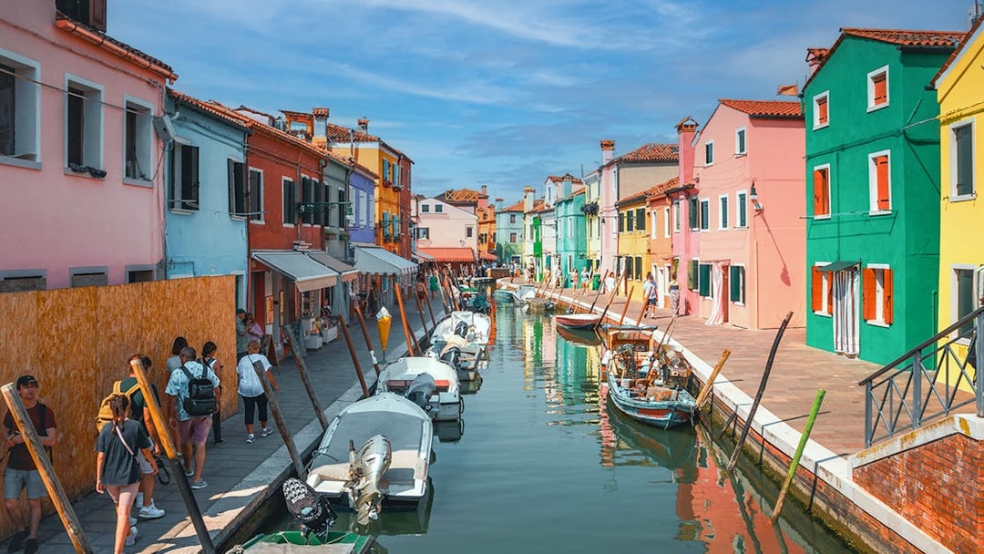 Colorful houses along Burano canal with people walking and boats docked.