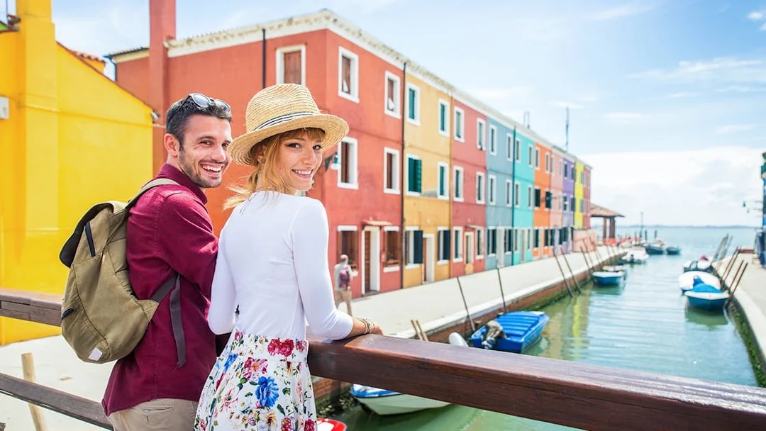 Couple walking along colorful canal in Burano, Italy.