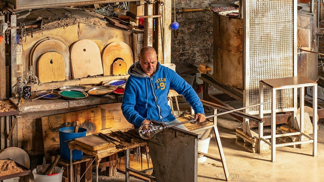 Artisan crafting glass at Murano workshop using traditional glass blowing techniques.
