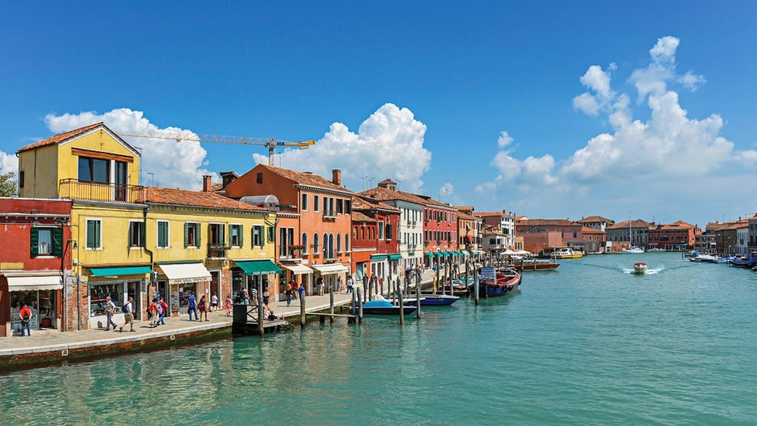 Colorful buildings along a canal in Murano, Italy, with boats and tourists.