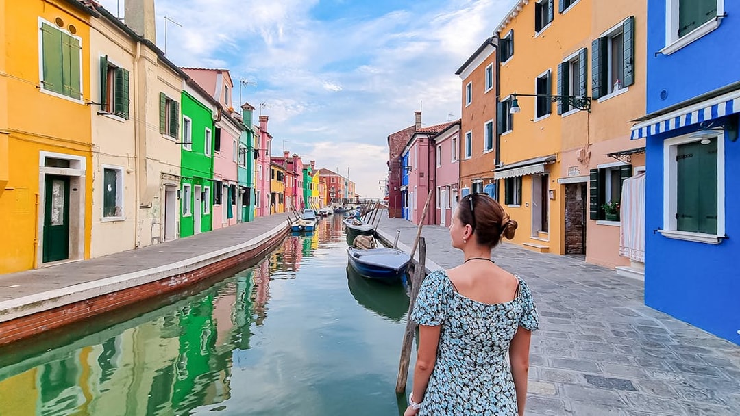 Tourist woman with hat viewing colorful houses along canal in Burano, Italy.