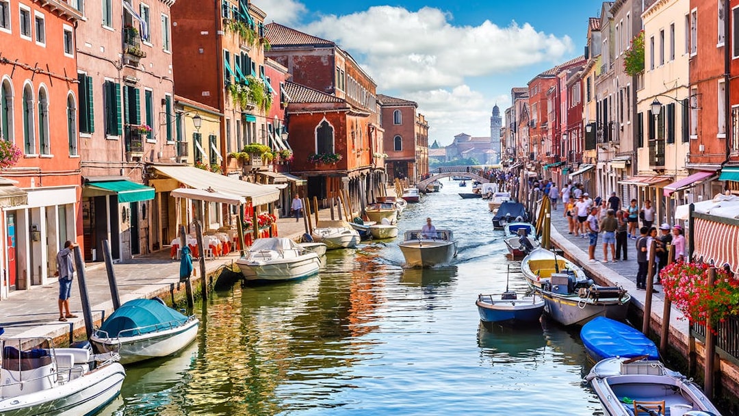 Canal with boats and colorful buildings on Murano Island, Venice, during a guided tour.