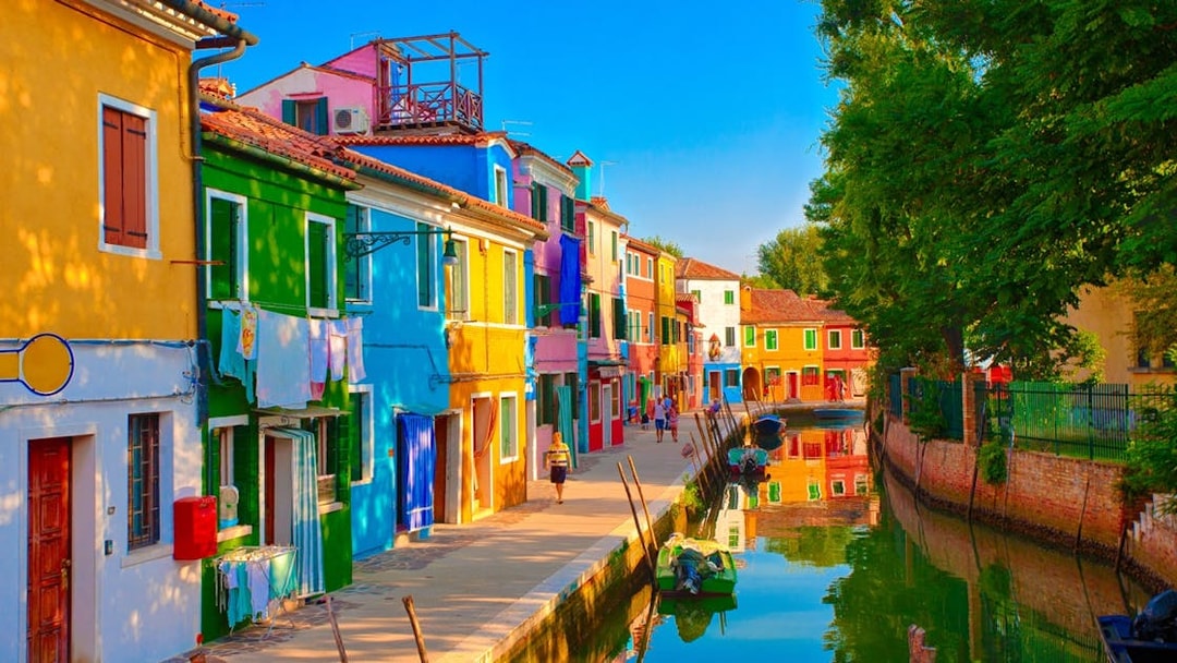Tourists walking along the colorful houses of Burano, Venice, near a canal.