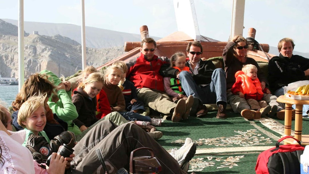 Group of people relaxing on a dhow cruise during Musandam Dibba tour with mountains in the background.