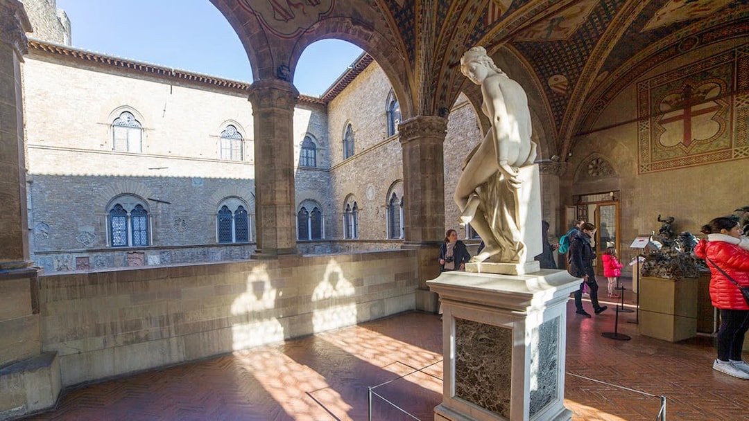 Statue in the courtyard of Museo del Bargello, Florence, with visitors exploring exhibits.