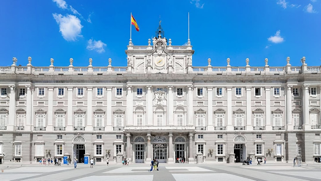 Royal Palace of Madrid facade with Spanish flag, highlighting its grand architecture.