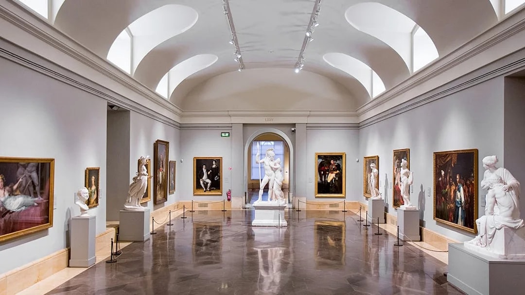 Interior of Prado Museum gallery with classical sculptures and paintings.