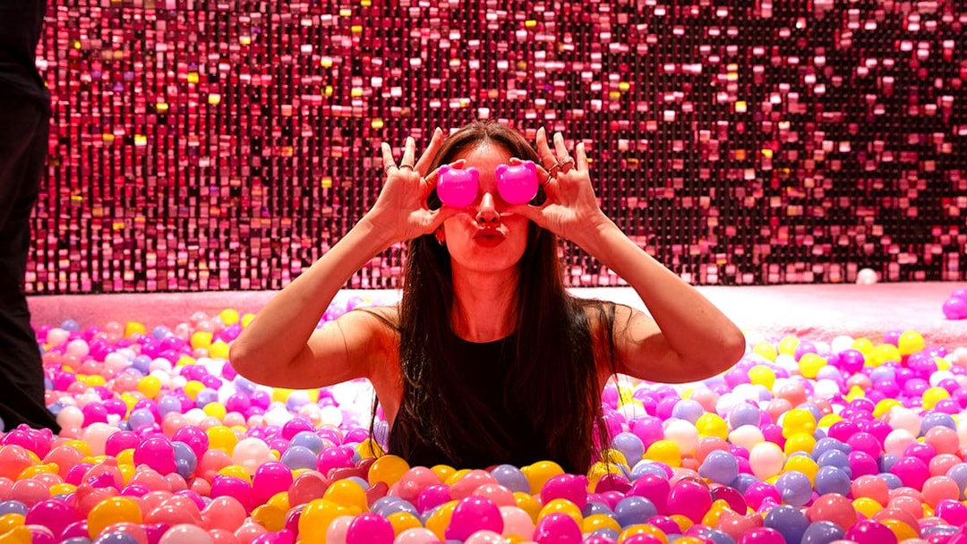 Visitor in Gummy Bear Pool at Museum of Candy, Dubai holding pink bears over eyes.