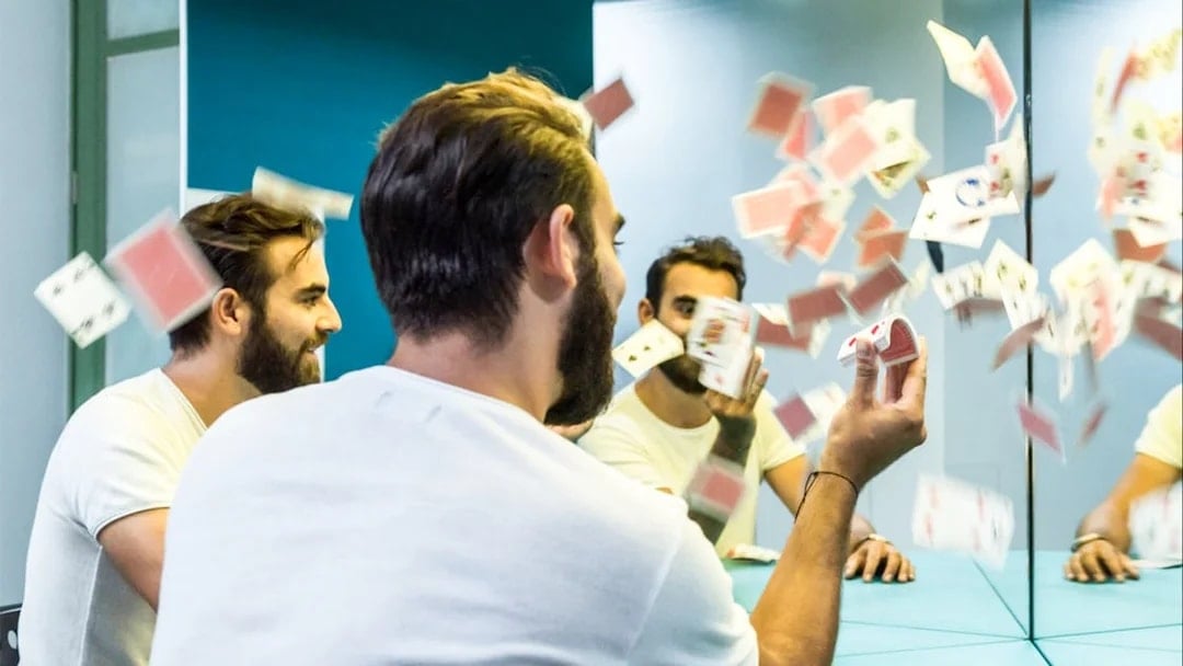 Man interacting with mirror illusion and playing cards at Museum of Illusions, Thessaloniki.