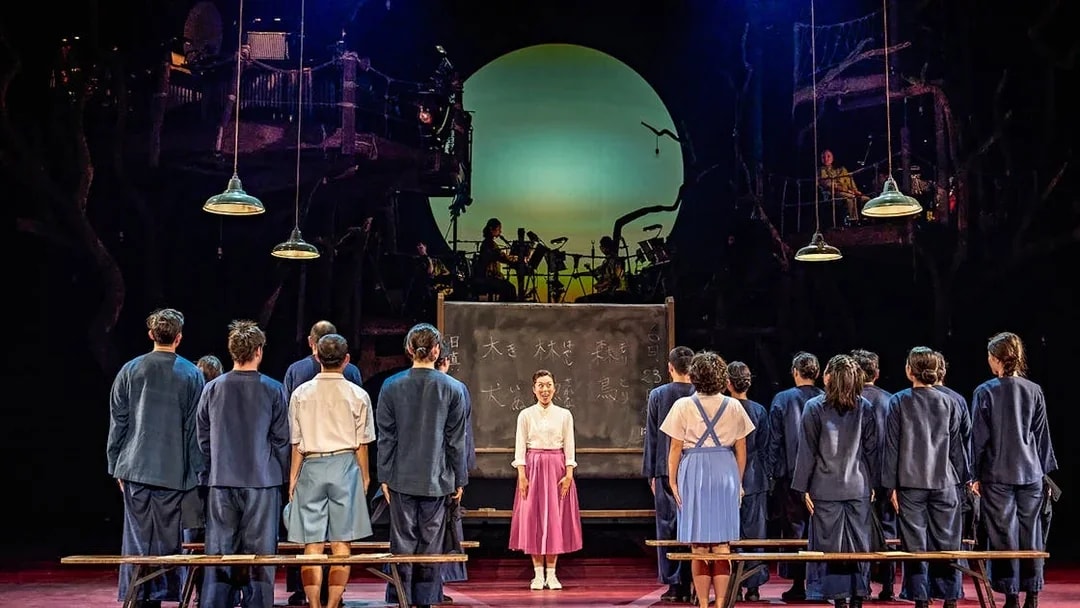 Stage performance of My Neighbour Totoro with actors in front of a chalkboard and musicians in the background.