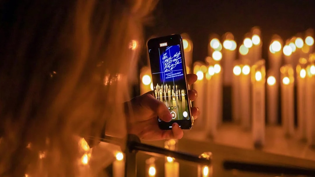 Person photographing candlelit scene with phone at Mythos Mozart event.