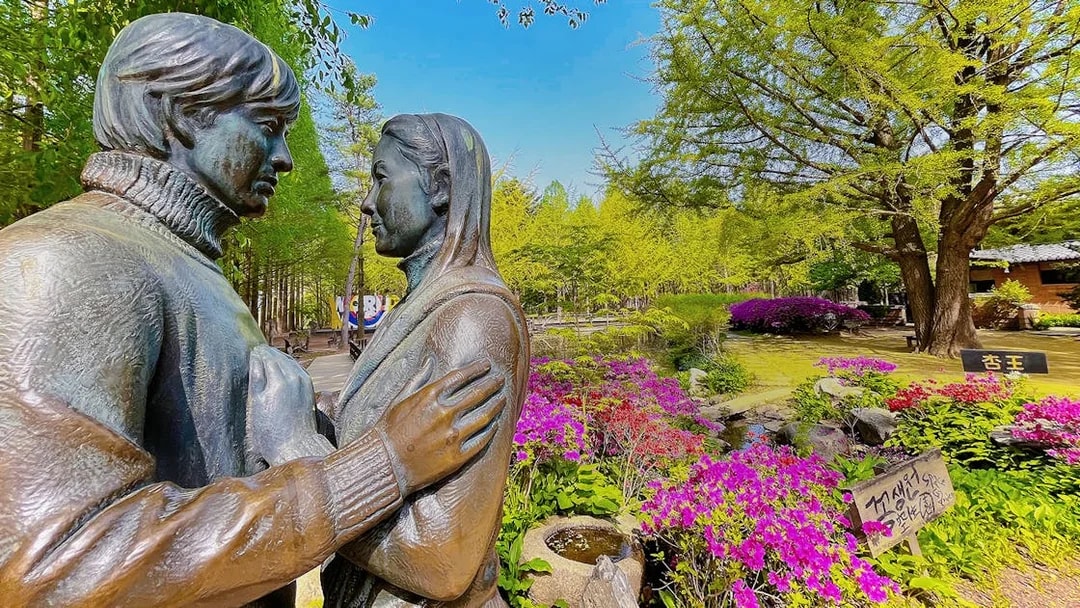 Statue of a couple surrounded by colorful flowers and trees on Nami Island, South Korea.