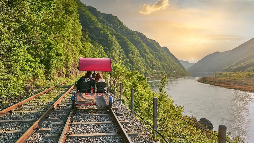 Couple on Gangchon Rail Bike along river track at sunset, South Korea.