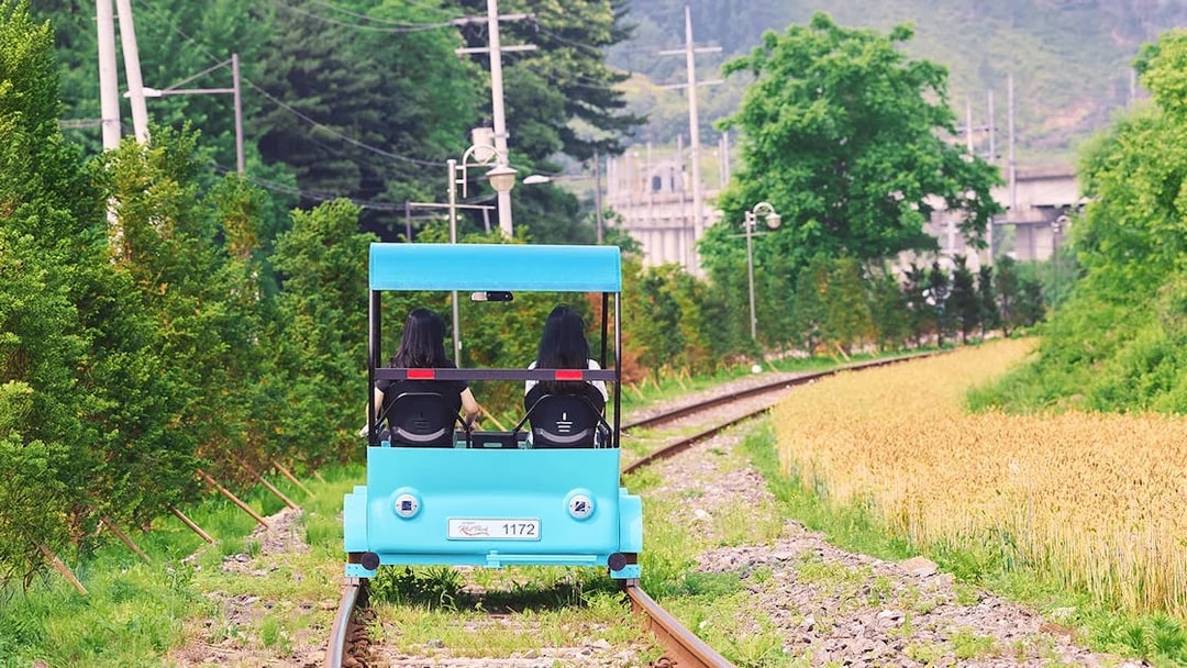 Two people riding a blue rail bike on tracks through countryside near Gapyeong, South Korea.