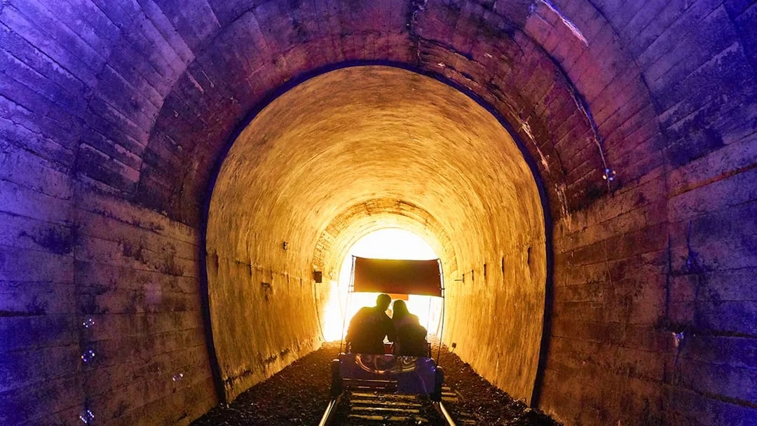 Couple on rail bike in illuminated tunnel, scenic track, South Korea.