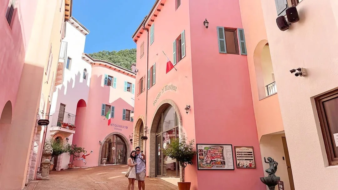 Couple in narrow cobblestone street between pink buildings at Italian Village, South Korea.